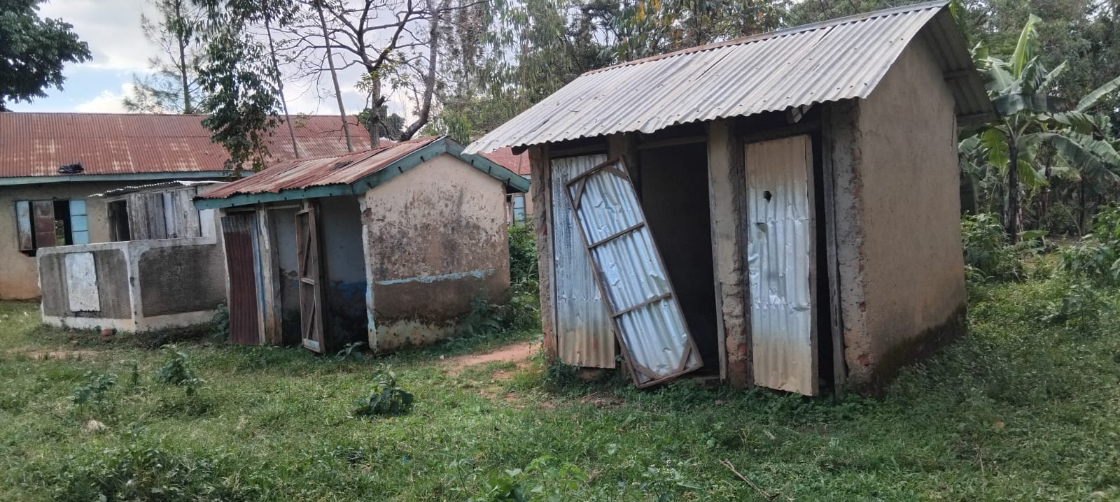 Old school latrines at Eshisenye Primary School with doors missing or falling from their frames